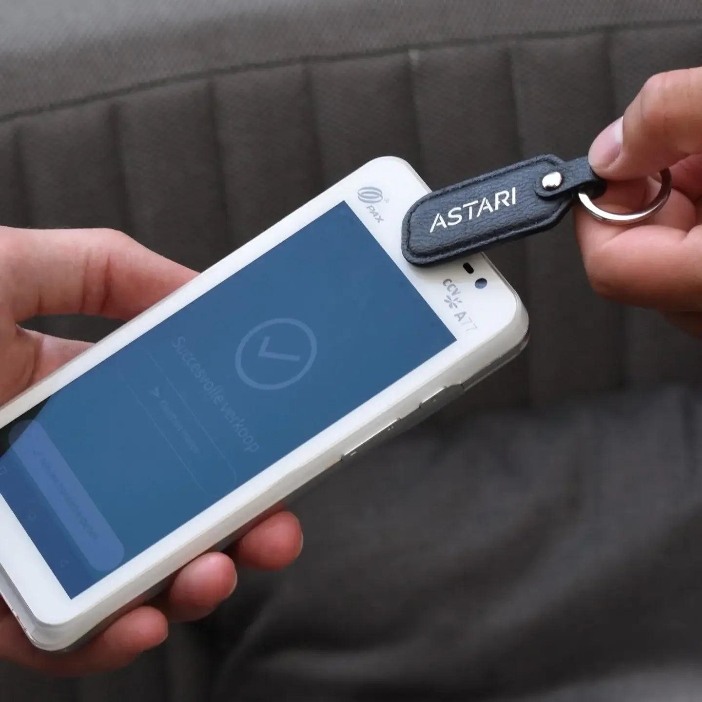 Close-up of a hand using an Astari keychain to make a contactless payment on a smartphone.
