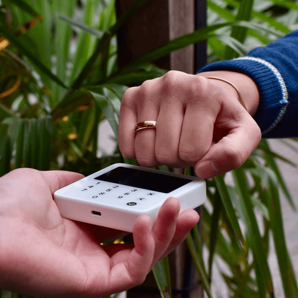 Person using a gold payment ring for contactless payment with a reader in a natural setting.