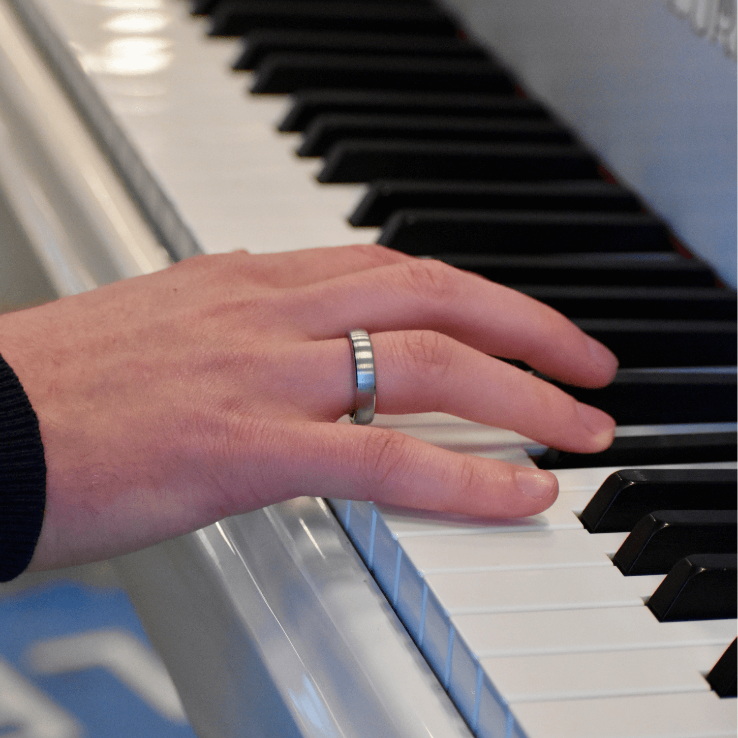 Hand wearing a sleek silver contactless payment ring while playing the piano on a white keyboard.